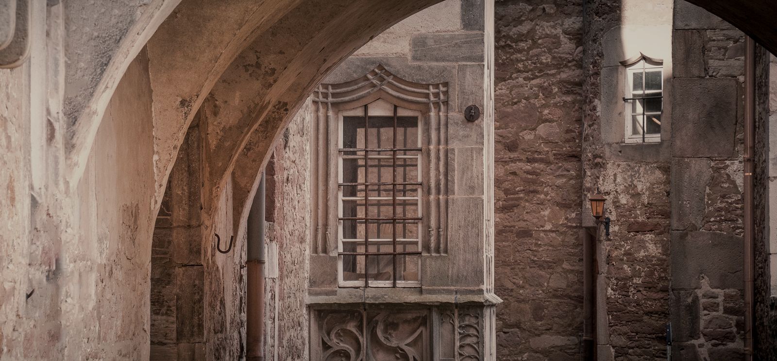 Blick durch einen alten Torbogen auf eine Steinfassade mit vergittertem Fenster